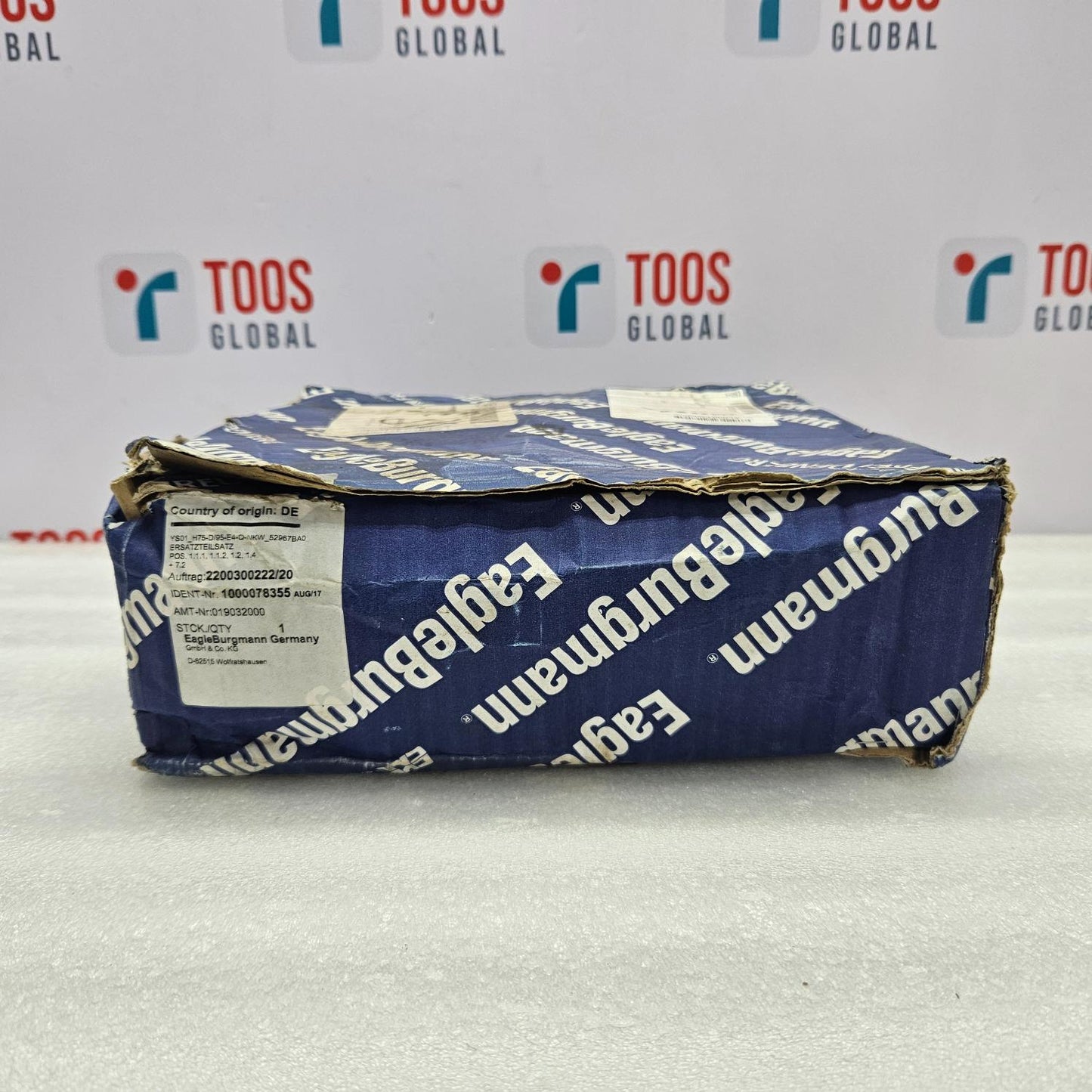 Blue package with 'Eagleburgmann' branding on a white surface with 'TOOS Global' logos in the background.