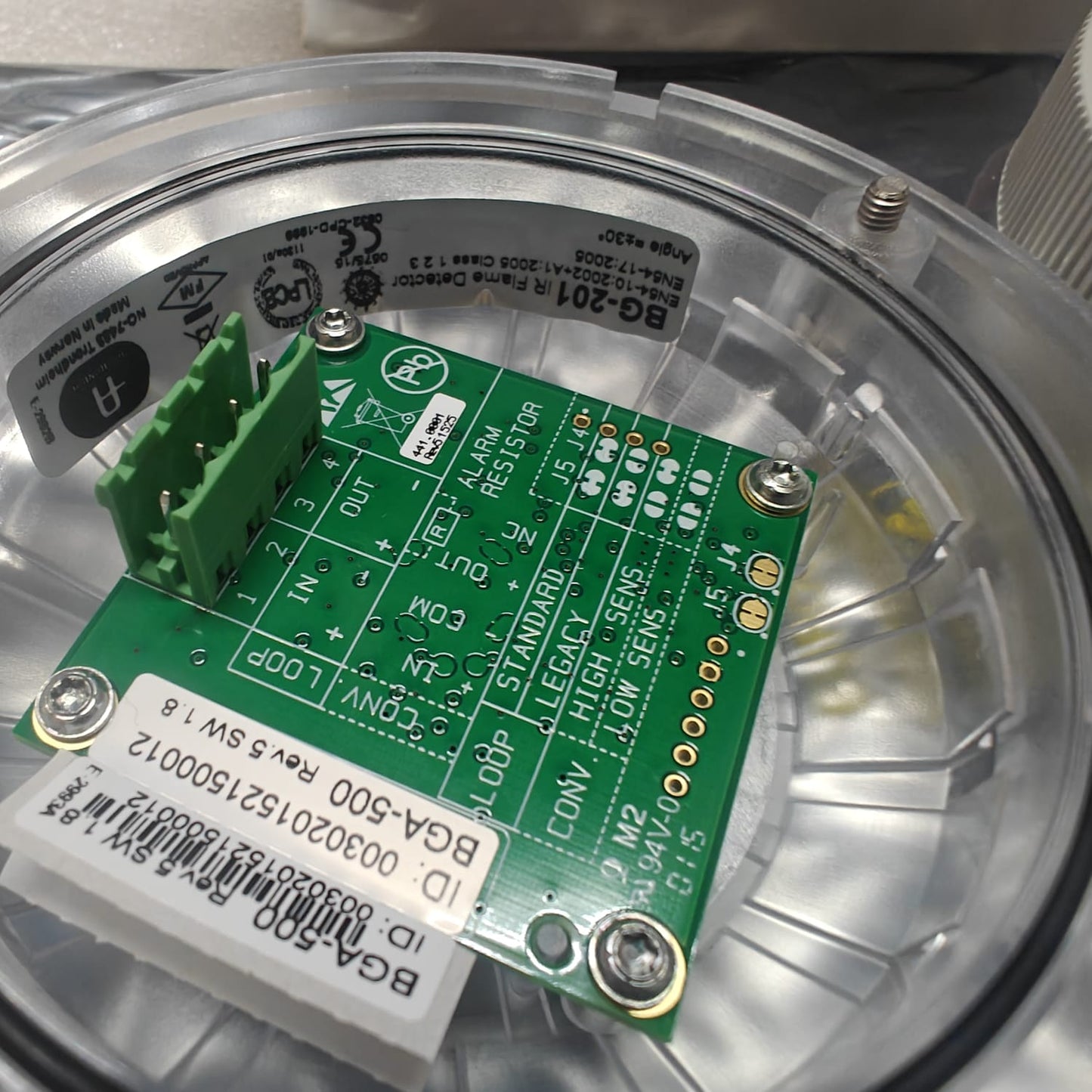 Close-up of a AUTRONICA 116-BG-201 green electronic circuit board with labels inside a transparent container.