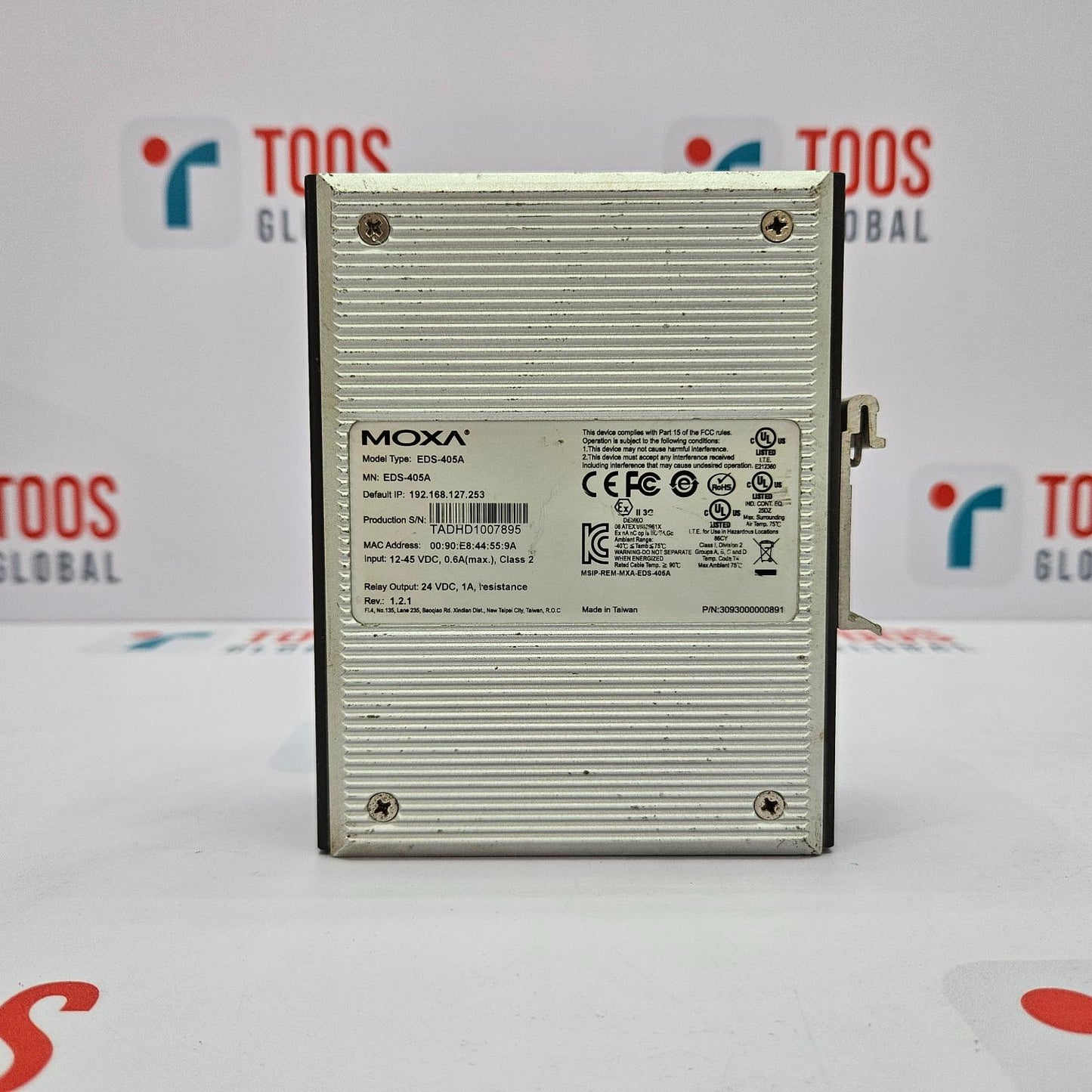 The image shows a MOXA EDS-405A Ethernet switch with 5 ports. The device is silver, with a metal casing and branding information visible on the front.