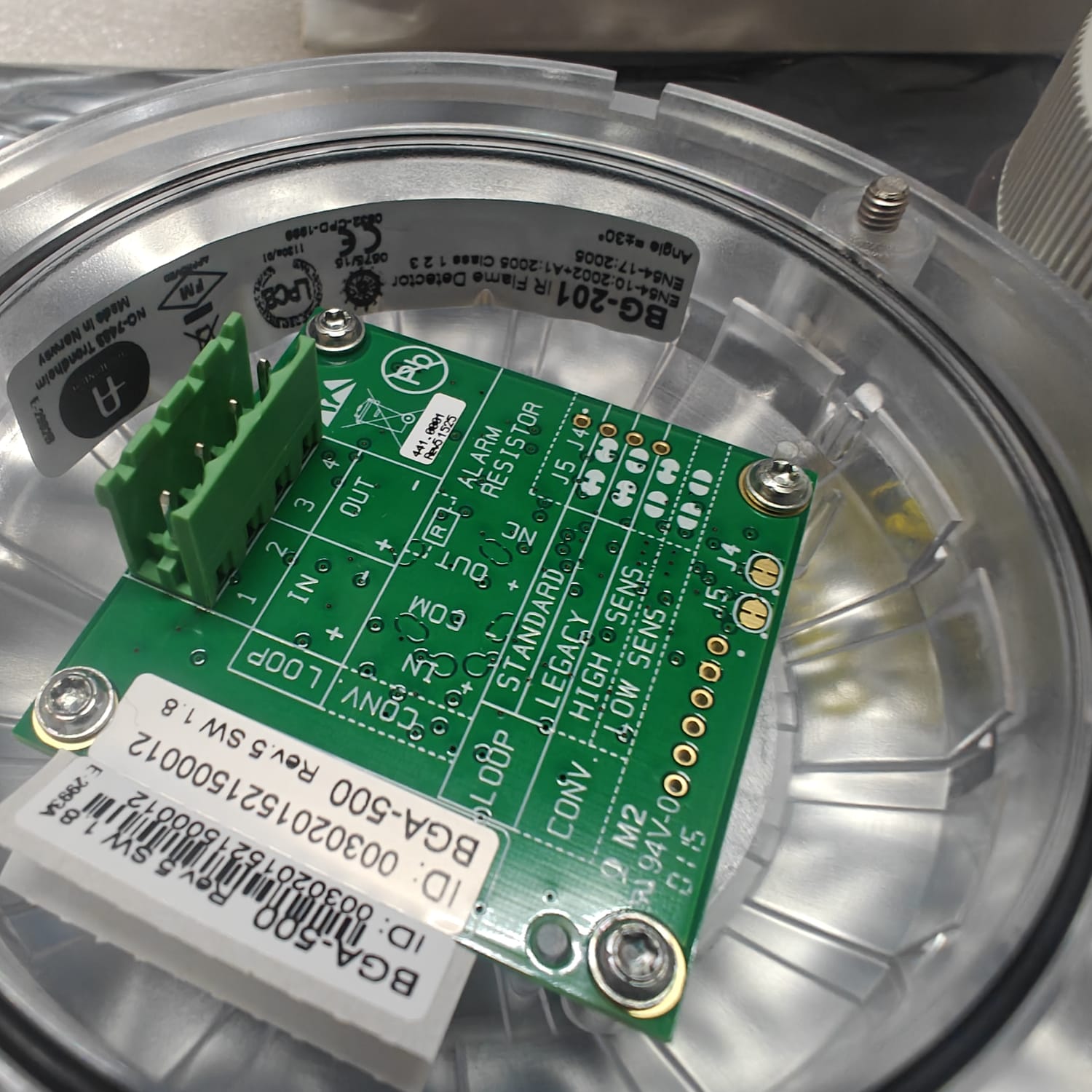 Close-up of a AUTRONICA 116-BG-201 green electronic circuit board with labels inside a transparent container.