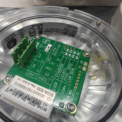Close-up of a AUTRONICA 116-BG-201 green electronic circuit board with labels inside a transparent container.