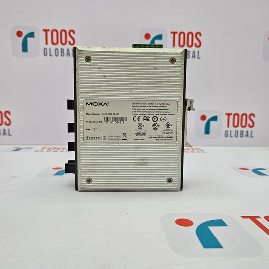 A MOXA EDS-308-M-SC 8-Port Unmanaged Ethernet Switch, with a silver body and black ports, positioned vertically on a table with a logo in the background.
