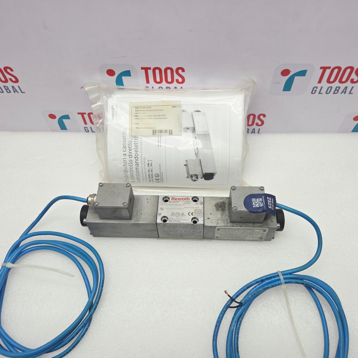 A Rexroth R901351579 4WE6J54/BG12-13NXHCKL/V Valve Hydac EX-1195-200 with blue cables connected to its terminals, shown in front of its plastic packaging and instruction manual. The background features a white surface and a branded backdrop with 'TOOS GLOBAL' logos.