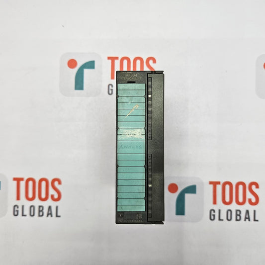Small rectangular object with a green and black pattern on a white background with 'TOOS GLOBAL' branding.