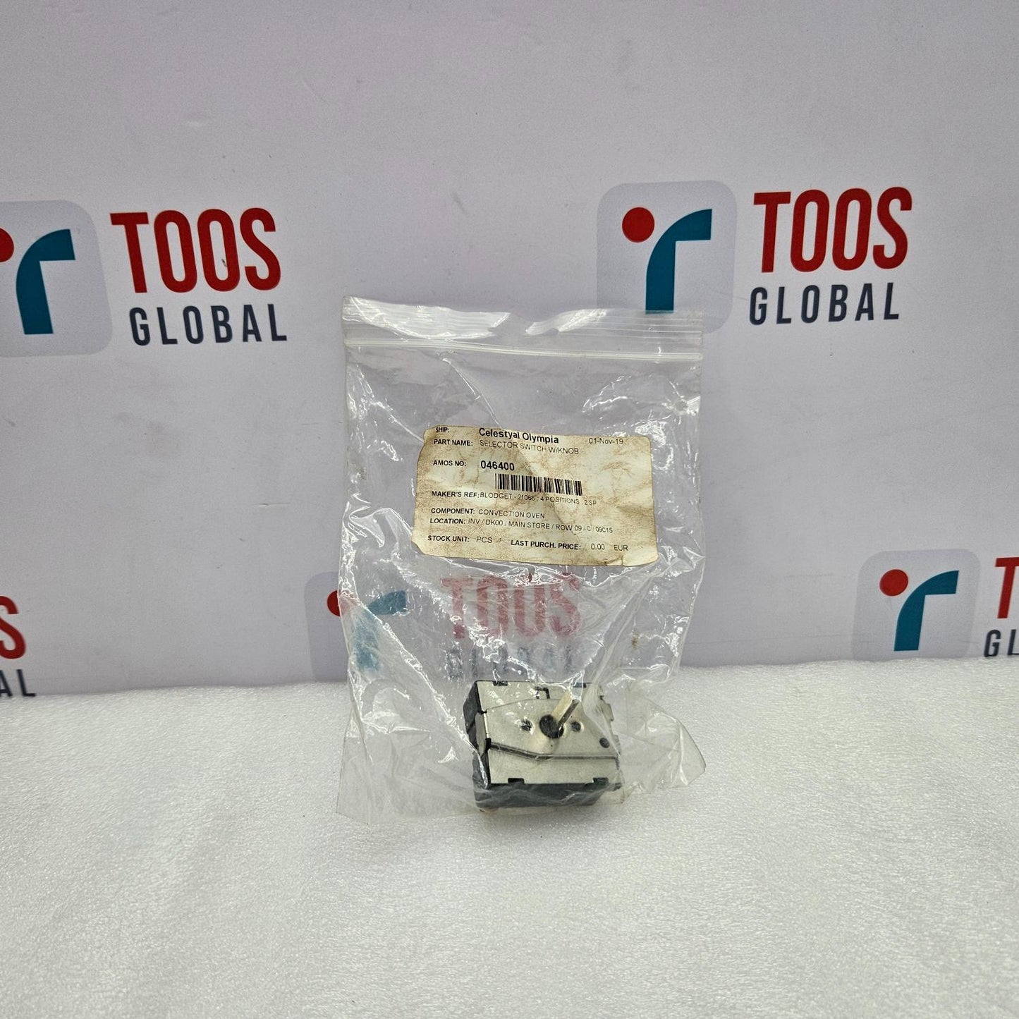 Small mechanical component in a clear plastic bag with 'TOOS GLOBAL' branding in the background.